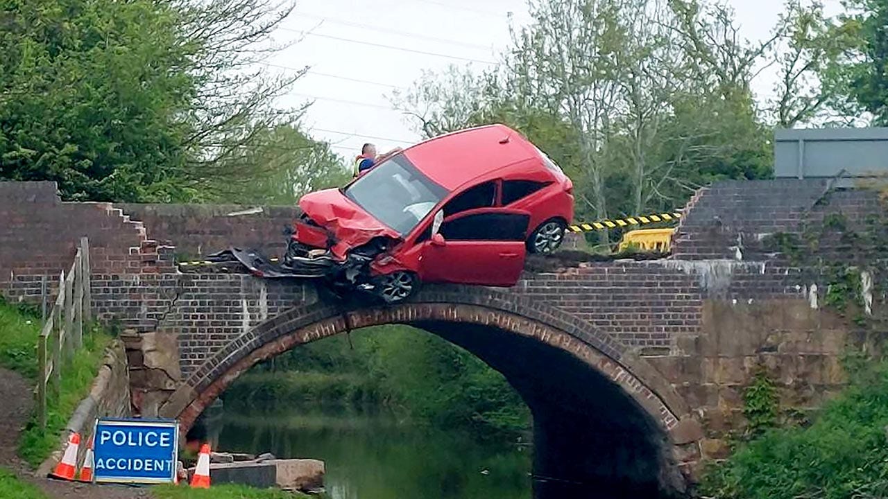 Featured image for Passenger's daring escape from car dangling over bridge into canal captured in dramatic photos.