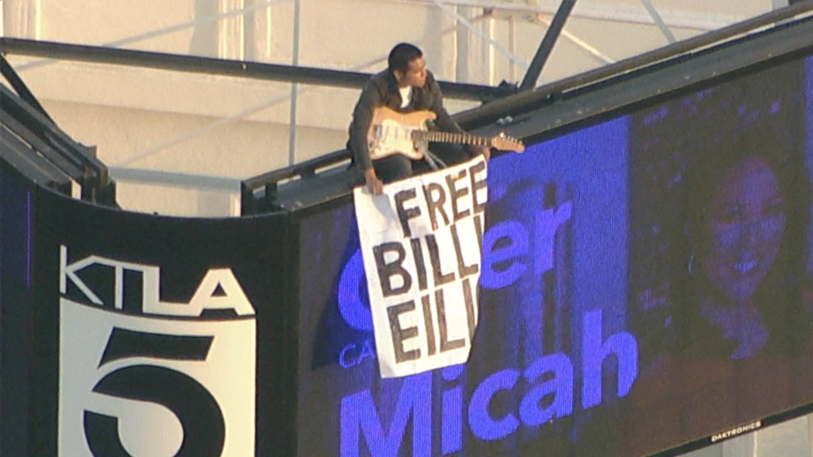 Man climbs KTLA tower in Hollywood with 'Free Billie Eilish' sign and guitar.