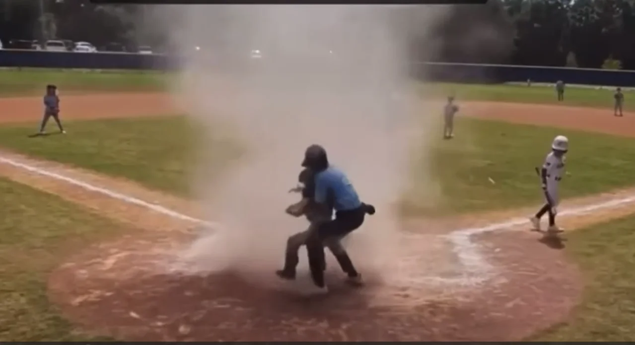 Umpire rescues child from dust devil during baseball game.